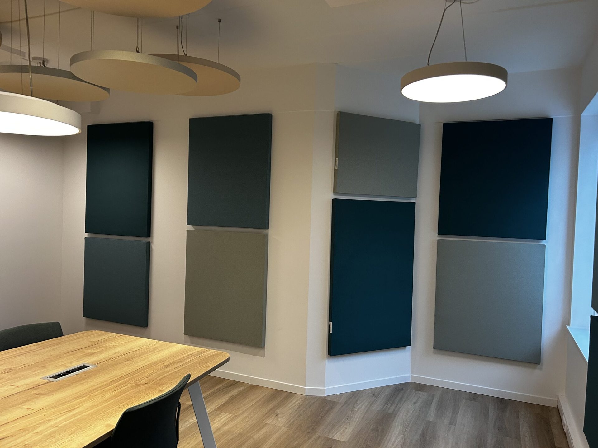 Vierkante akoestische wandpanelen in verschillende kleuren rond een vergadertafel